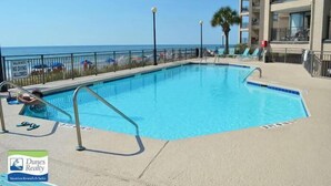 Una piscina con vistas a la playa, un área cercada y un edificio con balcones.