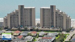 Un hotel de gran altura con varias plantas, vista al mar y un estacionamiento al frente.