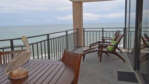 Un balcón con vista al océano, mobiliario de madera y una escultura decorativa.