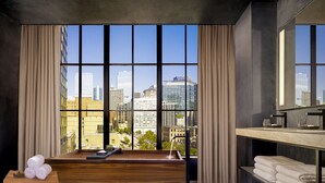 A modern hotel room with a large window, a wooden desk, a bathroom with a mirror, and a view of the cityscape. - Nobu Hotel Chicago (Chicago)
