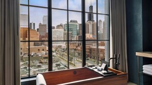 A modern hotel room with a large window offering a city view, a wooden desk with a laptop, and a small seating area. - Nobu Hotel Chicago (Chicago)