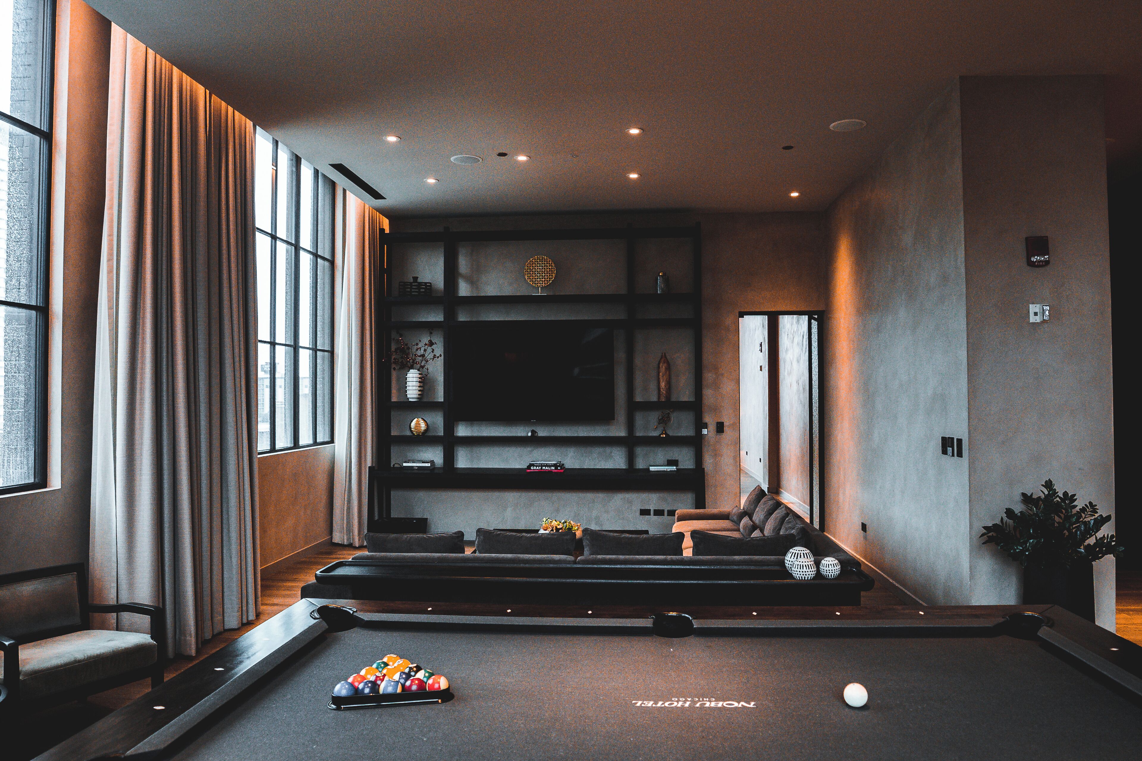 A modern living room with a pool table, comfortable seating, and a large window providing natural light.
