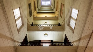 Un intérieur à plusieurs niveaux, doté d’un escalier central, de nombreuses fenêtres et d’un sol carrelé.