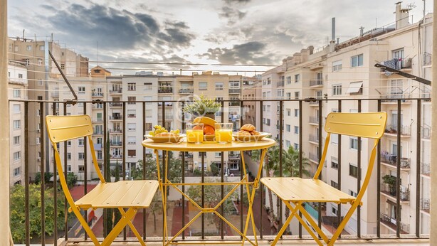 Un balcon avec des chaises jaunes et une table dressée avec de la nourriture et des boissons, donnant sur un quartier résidentiel.