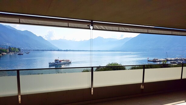 A balcony with a view of a lake, boats, and mountains.