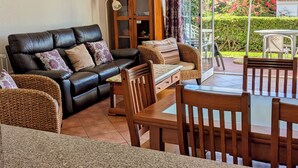 Een woonkamer met een leren bank, rieten stoelen, een houten tafel en een glazen kast.