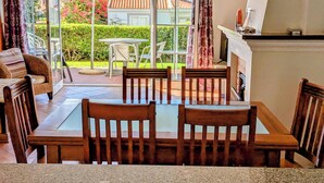 Een eetgedeelte met een glazen tafel, houten stoelen, een bank en een open haard.