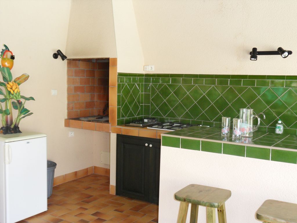 A compact kitchen with a built-in stove, a small refrigerator, and a green-tiled backsplash.