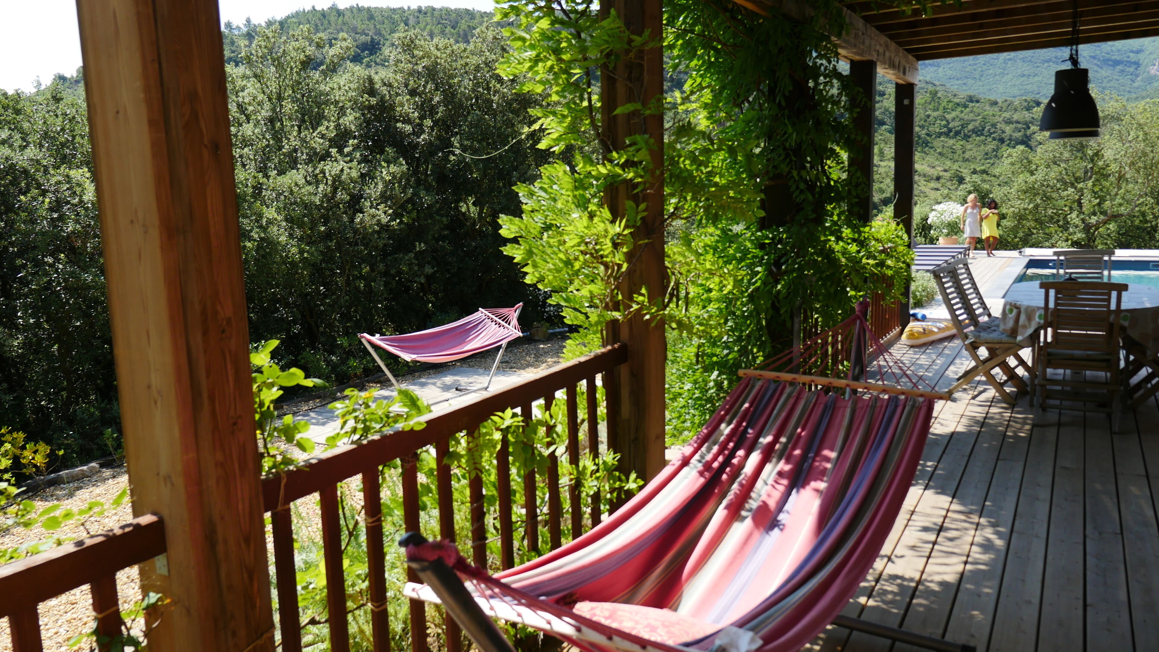 A wooden deck with a hammock, a pool, and a view of a forested area.