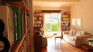 Una sala de estar acogedora con un sofá, una mesita de centro y una estantería llena de libros. Una ventana grande ofrece vistas a zonas verdes.