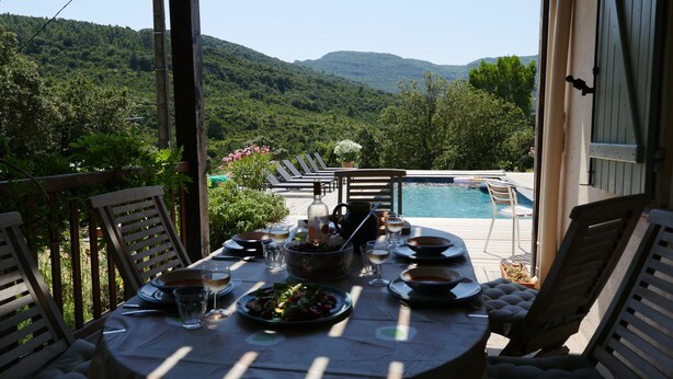Mesa de comedor para cuatro con vista a una piscina y montañas al fondo.