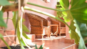 Wicker furniture arranged on a tiled patio with a pink building in the background. - Ose Cottages (Kisumu)