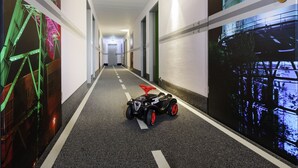Een gang met een speelgoedauto, muren met kleurrijke muurschilderingen en deuren langs de gang.