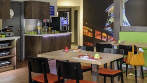Een modern restaurant met een bar, houten tafels en zwarte stoelen.