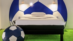 Een slaapkamer met een bed, een voetbal en een groen tapijt.