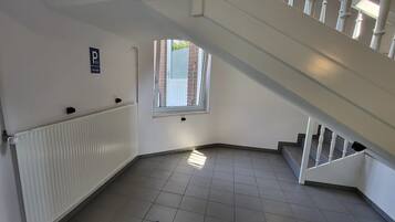 Un couloir en angle avec un radiateur, une fenêtre et un escalier.