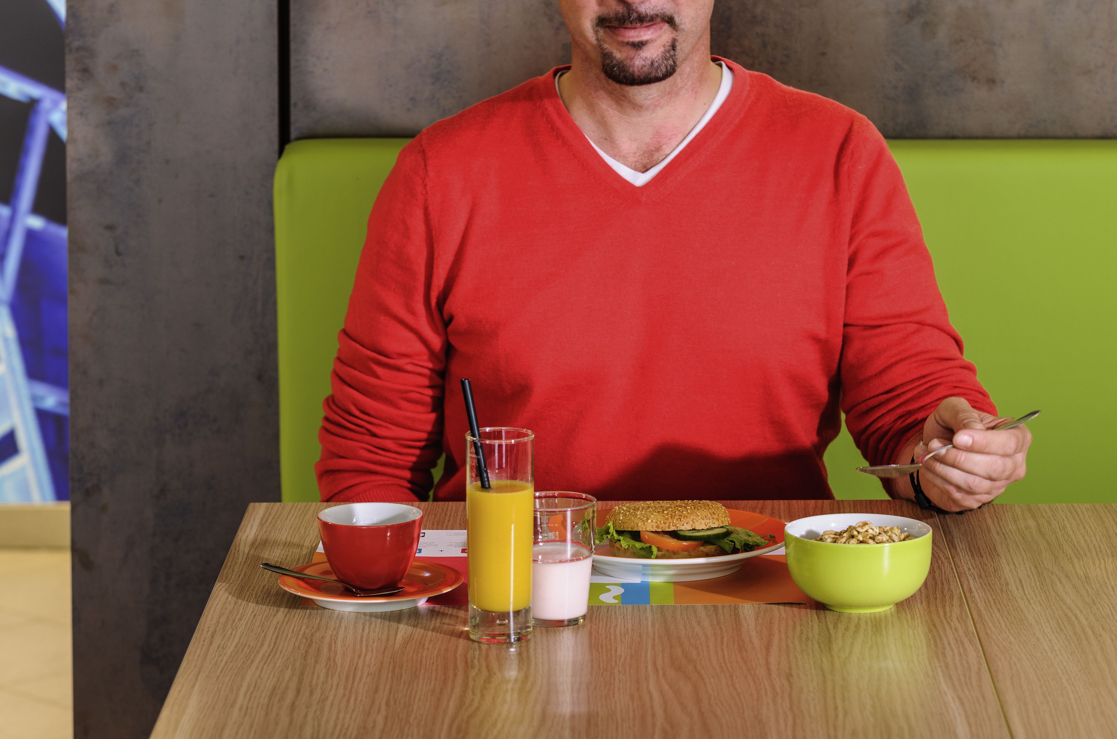 Una persona sentada a una mesa con una comida que incluye un sándwich, un tazón de cereal, un vaso de jugo de naranja y una taza de leche.