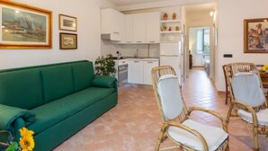 A living room with a green sofa, wicker chairs, a ceiling fan, and a kitchen in the background. - Michelangelo I by Interhome (Marina Pietrasanta)