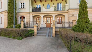 Ein Gebäude mit einem zentralen Eingang und Treppen, die hinaufführen, sowie einem Balkon im zweiten Stock.