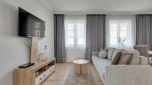 Ein modernes Wohnzimmer mit Flachbildfernseher, einer Holzeinrichtungsanlage, einem runden Couchtisch, einer Couch und einem großen Fenster mit Vorhängen.