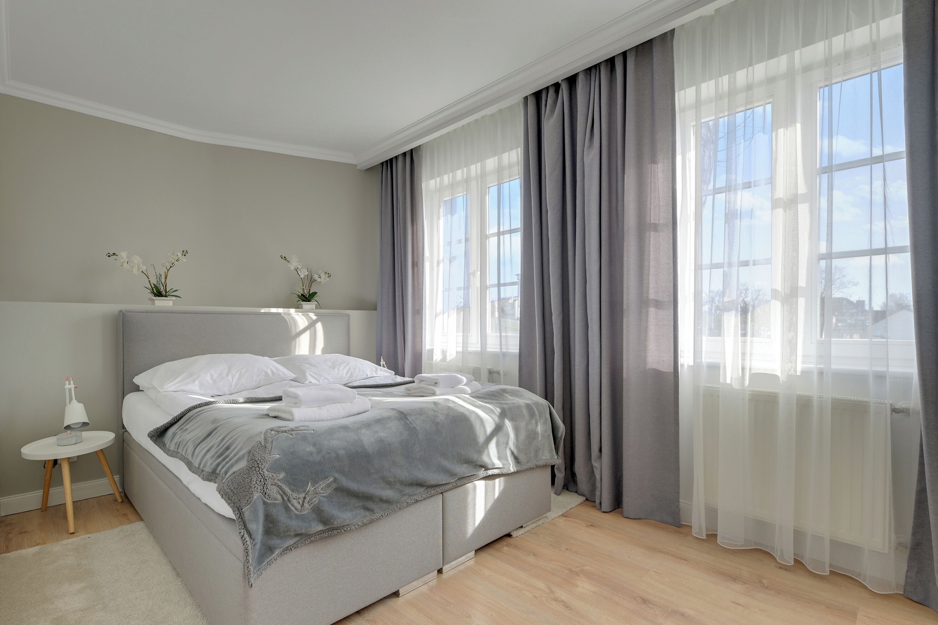 A modern bedroom with a bed, a bedside table, and sheer curtains.