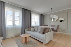 Una sala de estar moderna con un sofá, una mesa redonda de centro, una mesa de comedor, sillas y ventanas grandes con cortinas translúcidas.