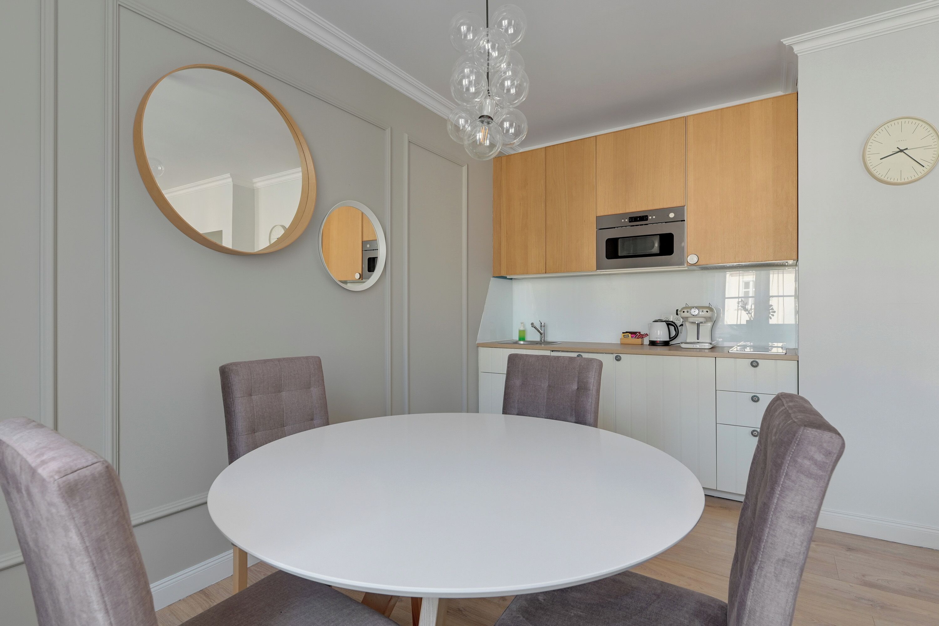 Una cucina moderna con mobili in legno, un piano di lavoro bianco e un tavolo da pranzo rotondo con quattro sedie.