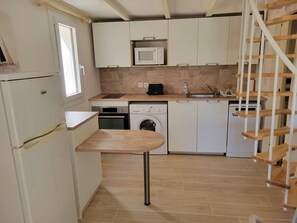 A compact kitchen with a washing machine, microwave, and a small wooden table. - Corner villa located in a secured residence with pool, for 4 people, at only 400m from the beach... (PORTIRAGNES)