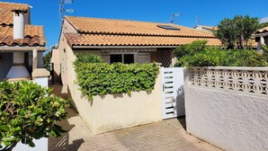 A residential building with a tiled roof, a white gate, and a hedge in front. - Corner villa located in a secured residence with pool, for 4 people, at only 400m from the beach... (PORTIRAGNES)