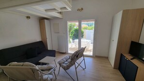 A living room with a sofa, two chairs, a TV, and a sliding glass door to an outdoor area. - Corner villa located in a secured residence with pool, for 4 people, at only 400m from the beach... (PORTIRAGNES)