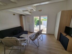A living room with a sofa, two chairs, a TV, and a sliding glass door to an outdoor area. - Corner villa located in a secured residence with pool, for 4 people, at only 400m from the beach... (PORTIRAGNES)