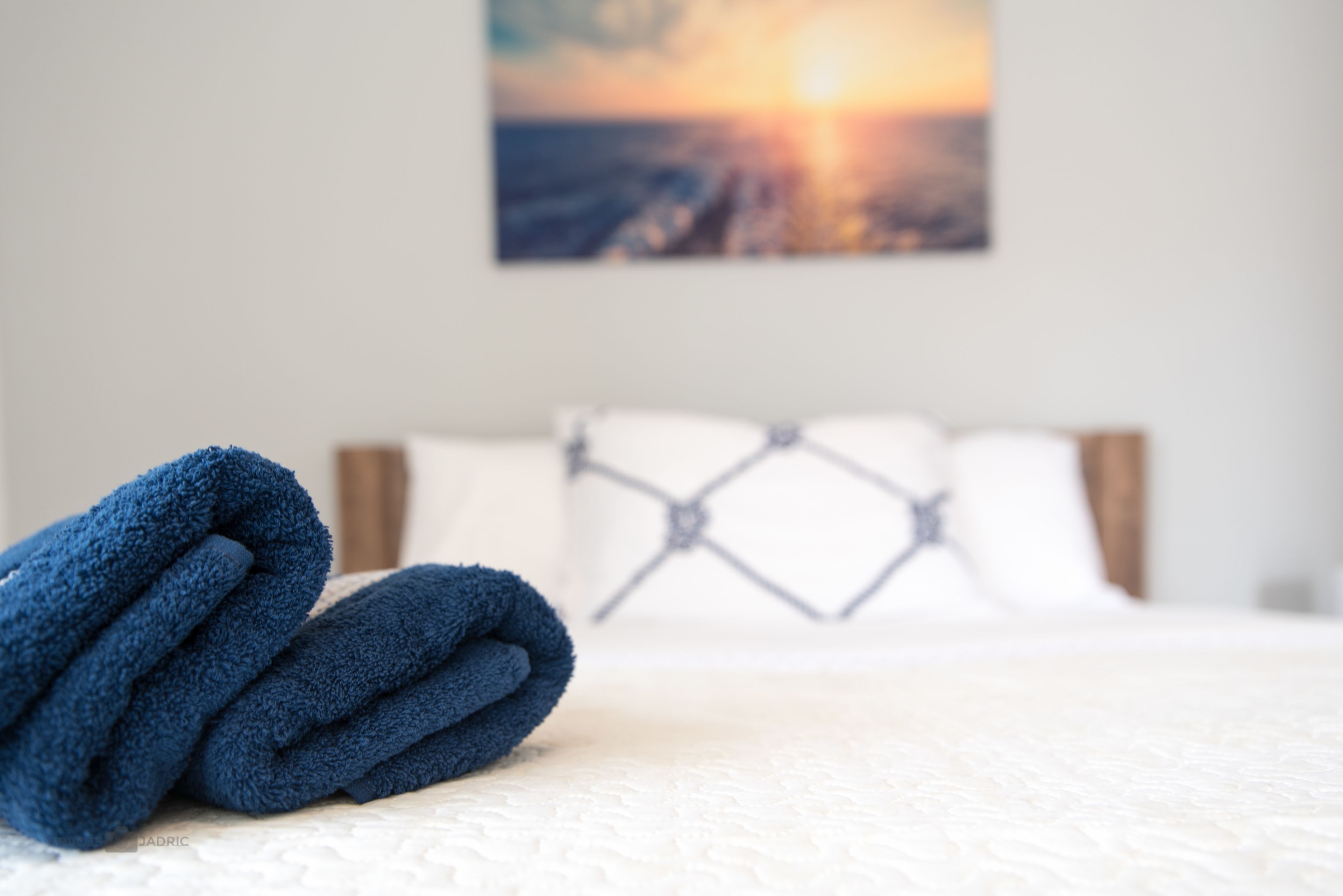 A neatly made bed with a white comforter and a blue towel folded on top.