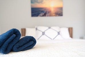 A neatly made bed with a white comforter and a blue towel folded on top. - Apartman Tonci (Primosten)