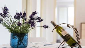 A table with a blue vase containing purple flowers and a wine bottle on a wire stand. - Apartman Tonci (Primosten)