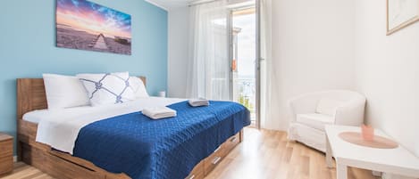 Un dormitorio con una cama de madera, una colcha azul, una silla blanca y un cuadro de una playa.