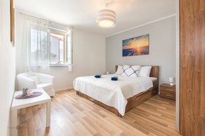 A bedroom with a bed, bedside table, chair, and a window with curtains. - Apartman Tonci (Primosten)