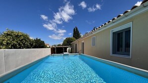 Una piscina con agua azul cristalina, rodeada por un edificio color beige con techo de tejas y ventanas.