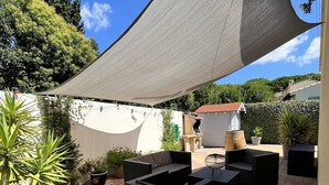 Un área de patio al aire libre con muebles de mimbre negro, plantas en macetas y una pared blanca.