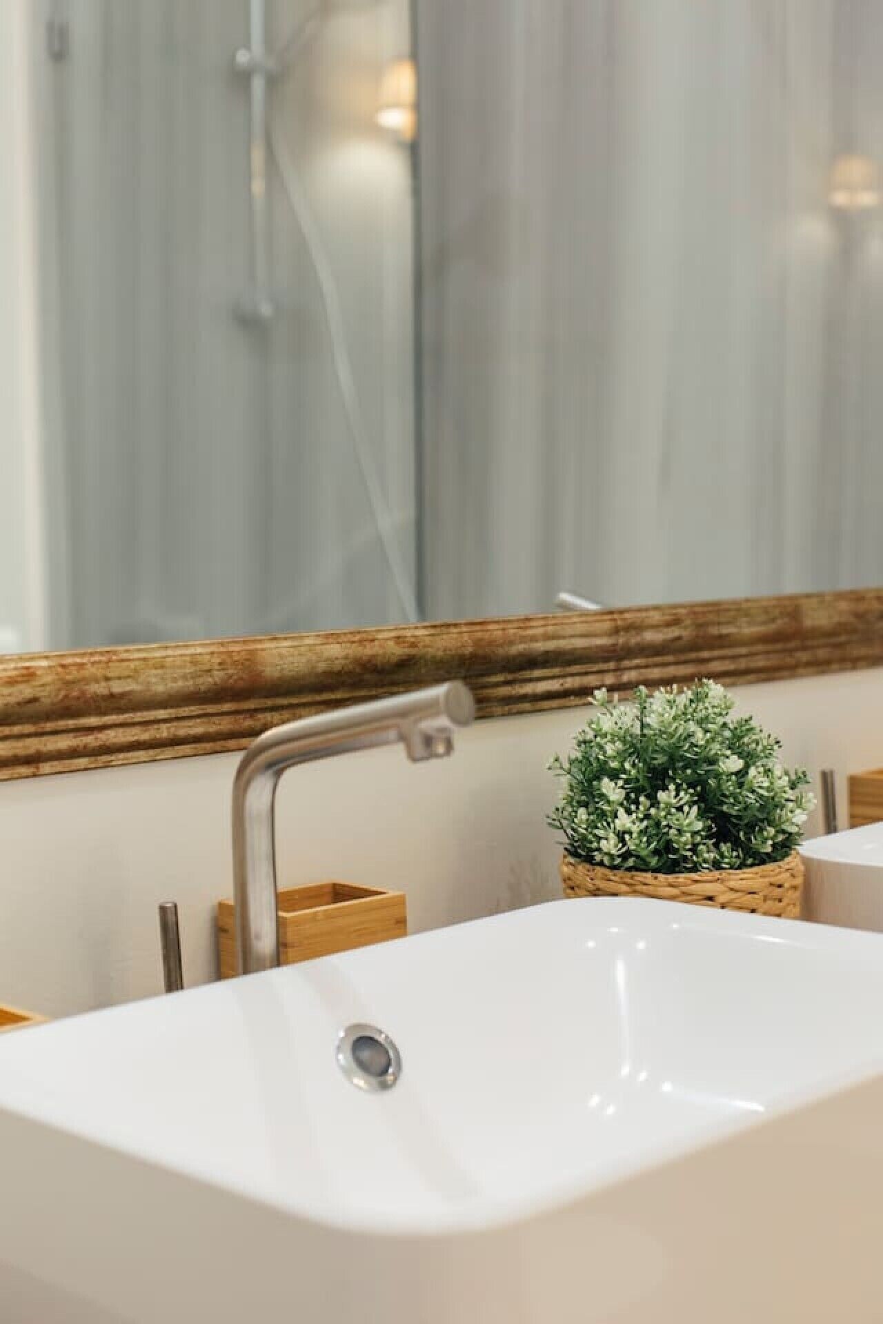 Un baño con un lavamanos blanco, un espejo con marco de madera y una pequeña planta en maceta.