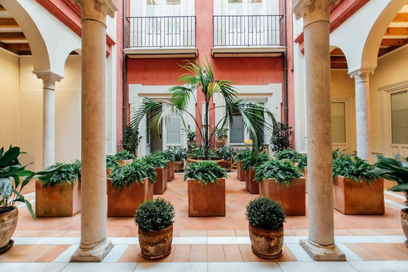 A courtyard with multiple potted plants, columns, and a central balcony.