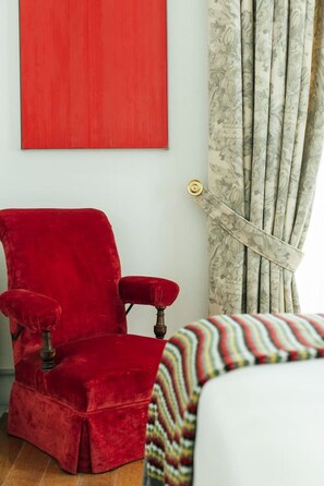 Een rode fluweelstoel, een wit bed en een rode wand met een groot, rood kunstwerk.