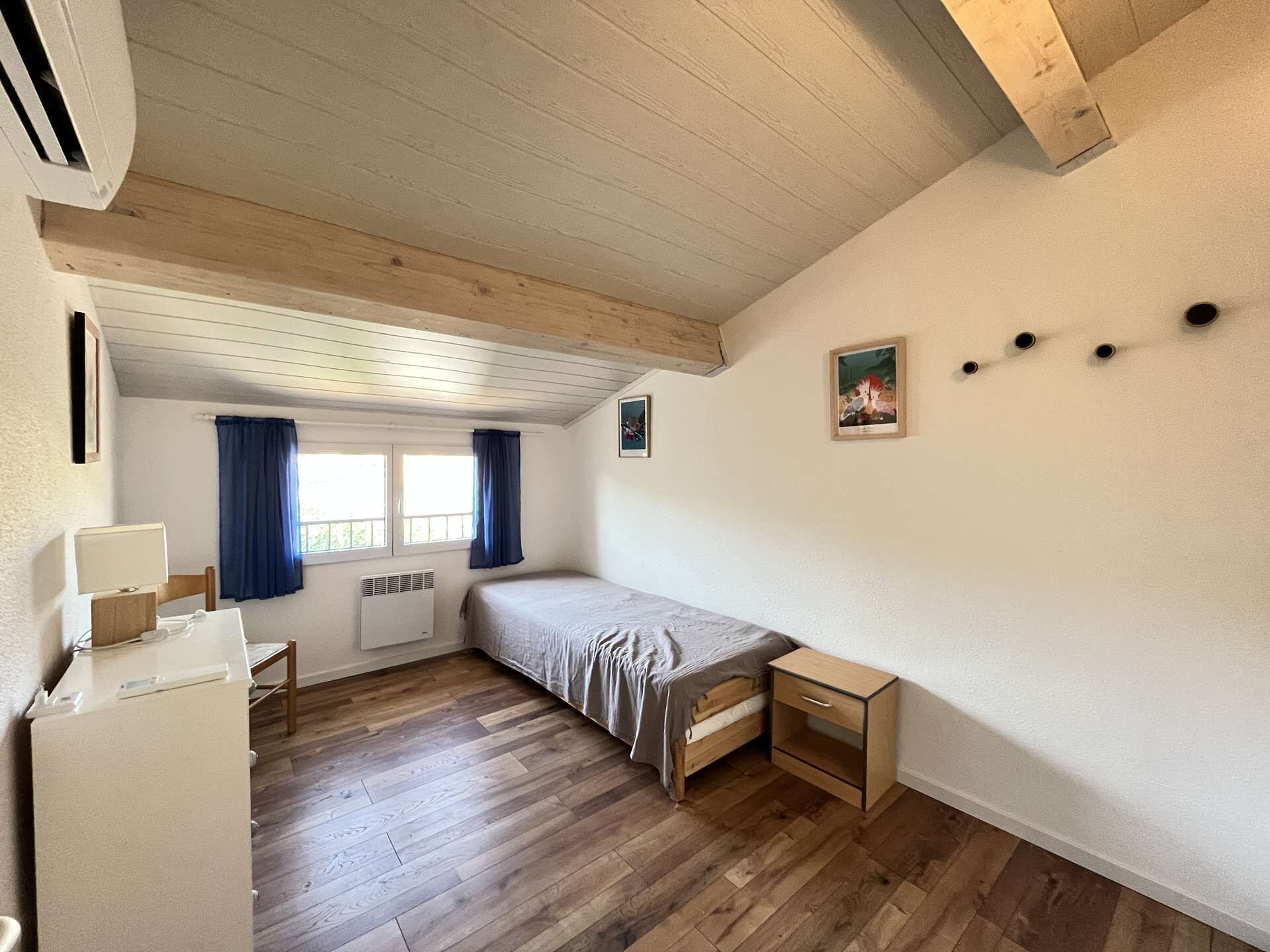 Quarto pequeno e acolhedor com soalho de madeira, uma cama, uma escrivaninha e um radiador.