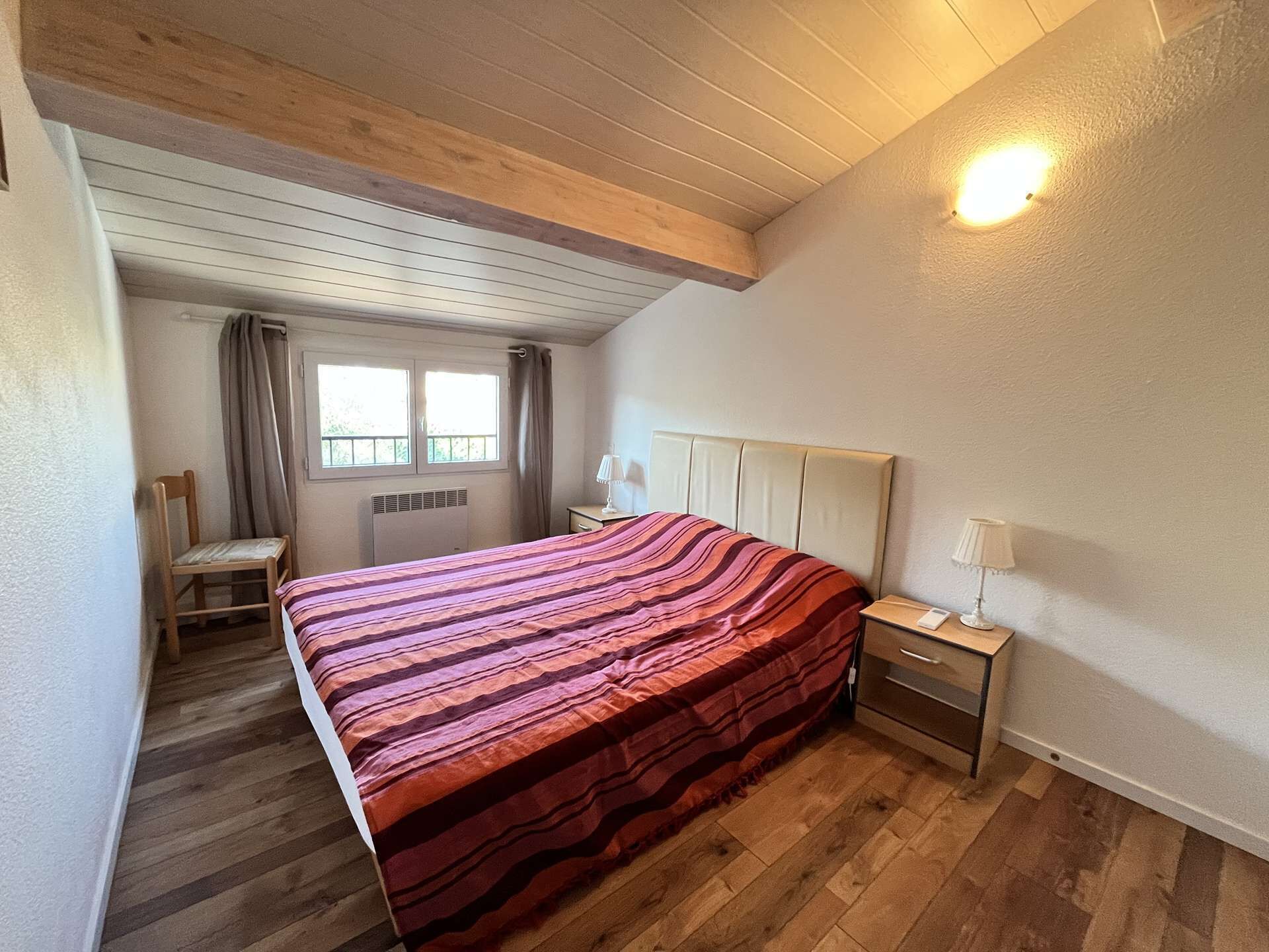 Ein Schlafzimmer mit Bett, Sessel, Nachttisch, Lampe, Fenster und Deckenleuchte.