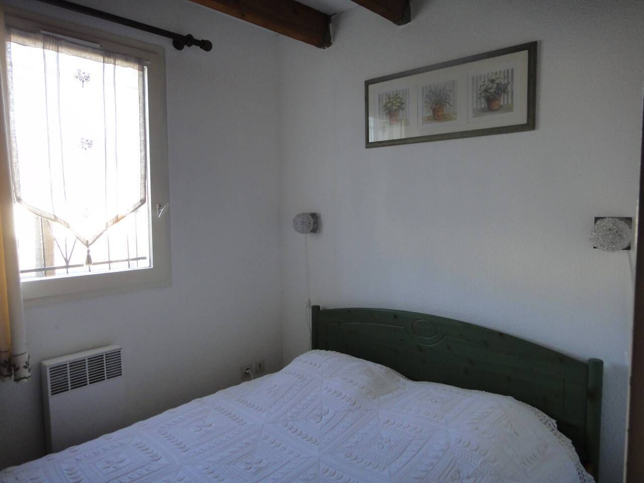 A bedroom with a single bed, a window with curtains, a radiator, and a framed picture on the wall.
