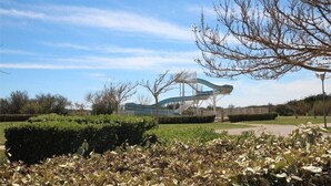 Un parque con una escultura moderna, arbustos bien cuidados y un cielo despejado.