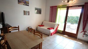 Una habitación con una mesa de comedor de madera, un sofá con cojines rojos, un televisor y un ventanal corredero que da a un espacio al aire libre.