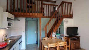 Una cocina con escalera de madera, zona de comedor con mesa y sillas, televisor y microondas.
