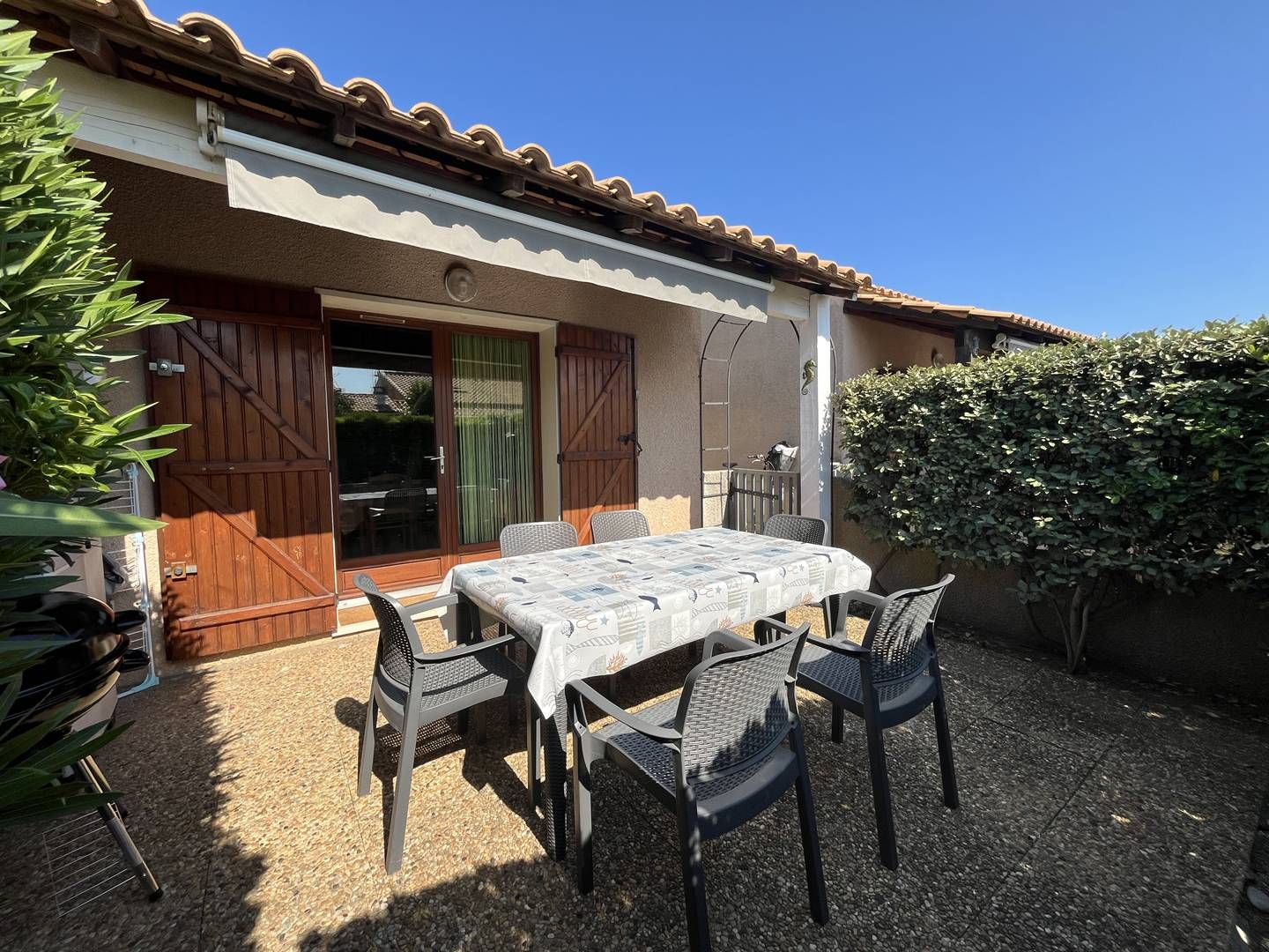 Une terrasse extérieure avec une table et des chaises, une porte en bois et un espace abrité.