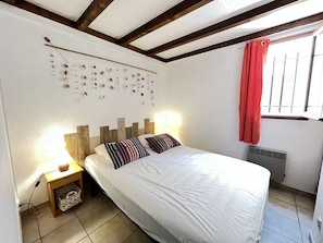A bedroom with a bed, bedside table, wall decor, and a window with curtains.
