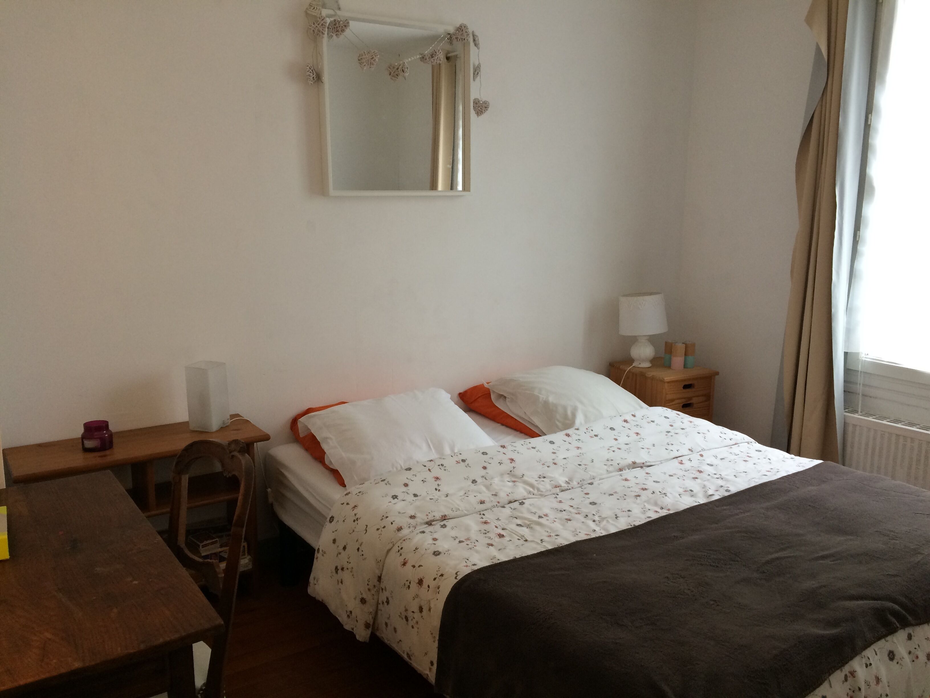 Ein Hotelzimmer mit Bett, Nachttisch, Lampe und einem Fenster mit Vorhängen.
